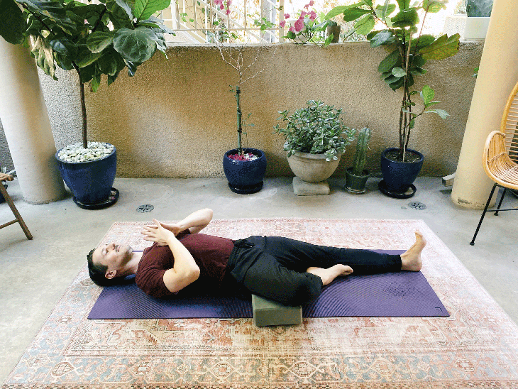 Man lying on his back on a yoga mat with one leg straight and the other knee bent in Tree Pose
