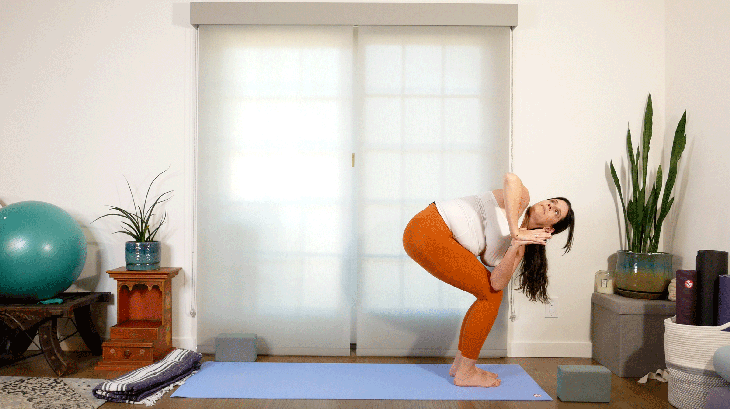 Woman standing at the front of a yoga mat with her feet together and her knees bent twisting to the right