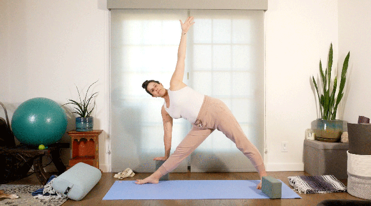 Woman on her yoga mat practicing Triangle Pose with block in a restorative yoga approach with her right hand supported
