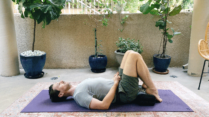 Man lying on a yoga mat on his back with his knees bent and his heels resting on a block.