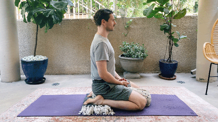 Man sitting on a bolster or pillow with his knees bent and his heels by his hips.