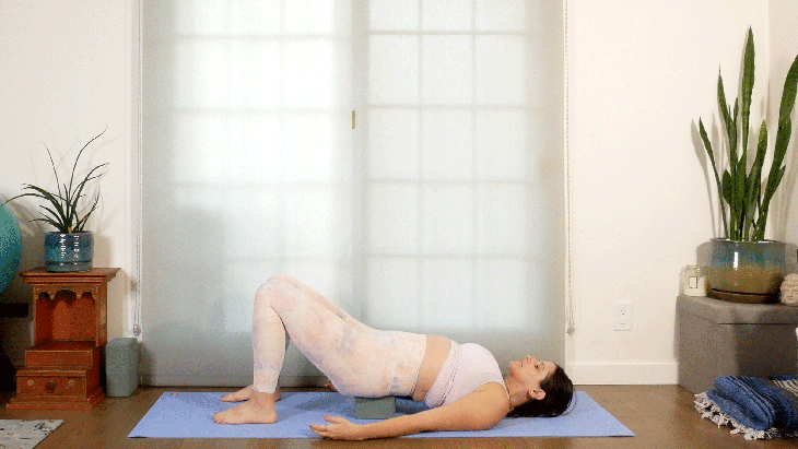 Woman lying on her back in Bridge Pose with a yoga block beneath her sacrum in a supported restorative version of the pose