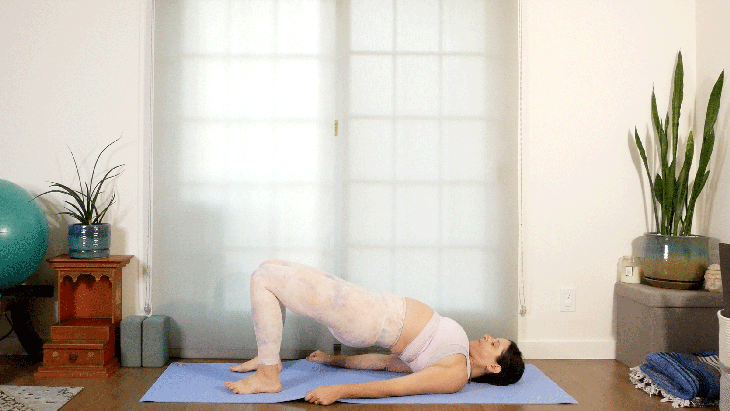Woman lying on her yoga mat practicing Bridge Pose and holding onto the edges of the yoga mat