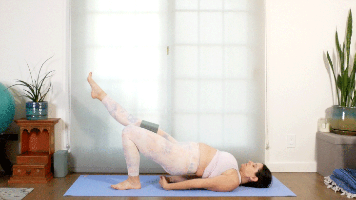 Woman lying on her back in a yoga pose with one leg extended in the air toward the front of the mat and the other leg bent with her foot on the mat