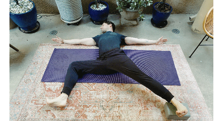 May lying on a yoga mat practicing a reclined version of Warrior 2 Pose