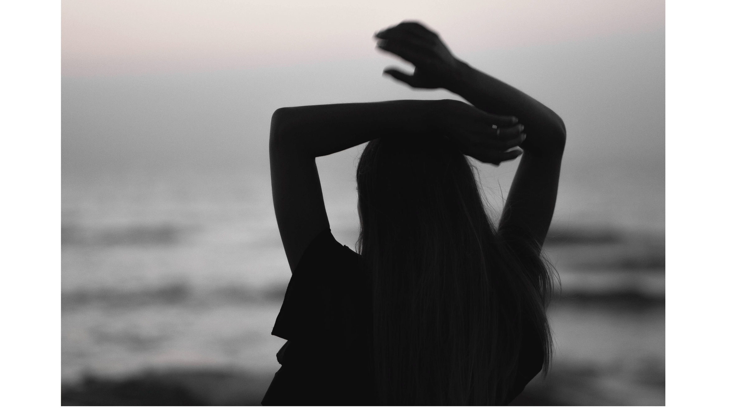Woman standing on the beach beneath a full moon with her arms above her head dancing