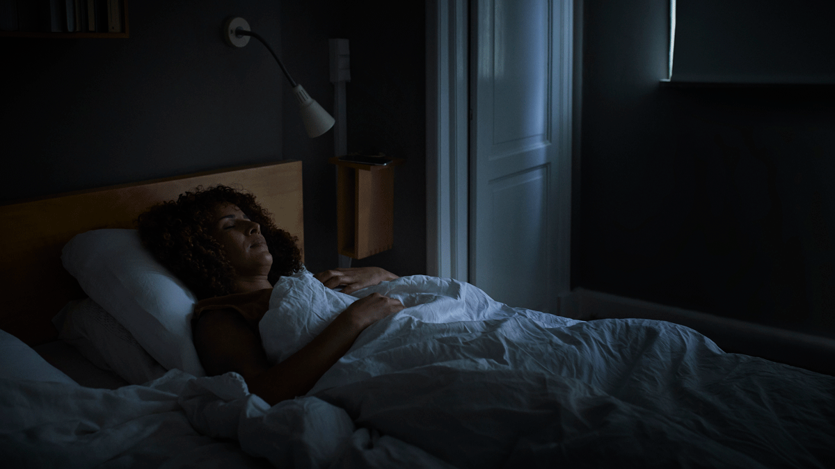 Woman lying in bed in a dark room learning how to sleep better by chanting