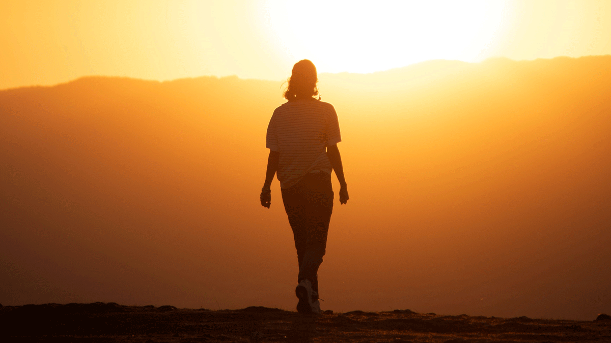 Woman on a hike walking toward mountains and the sunrise