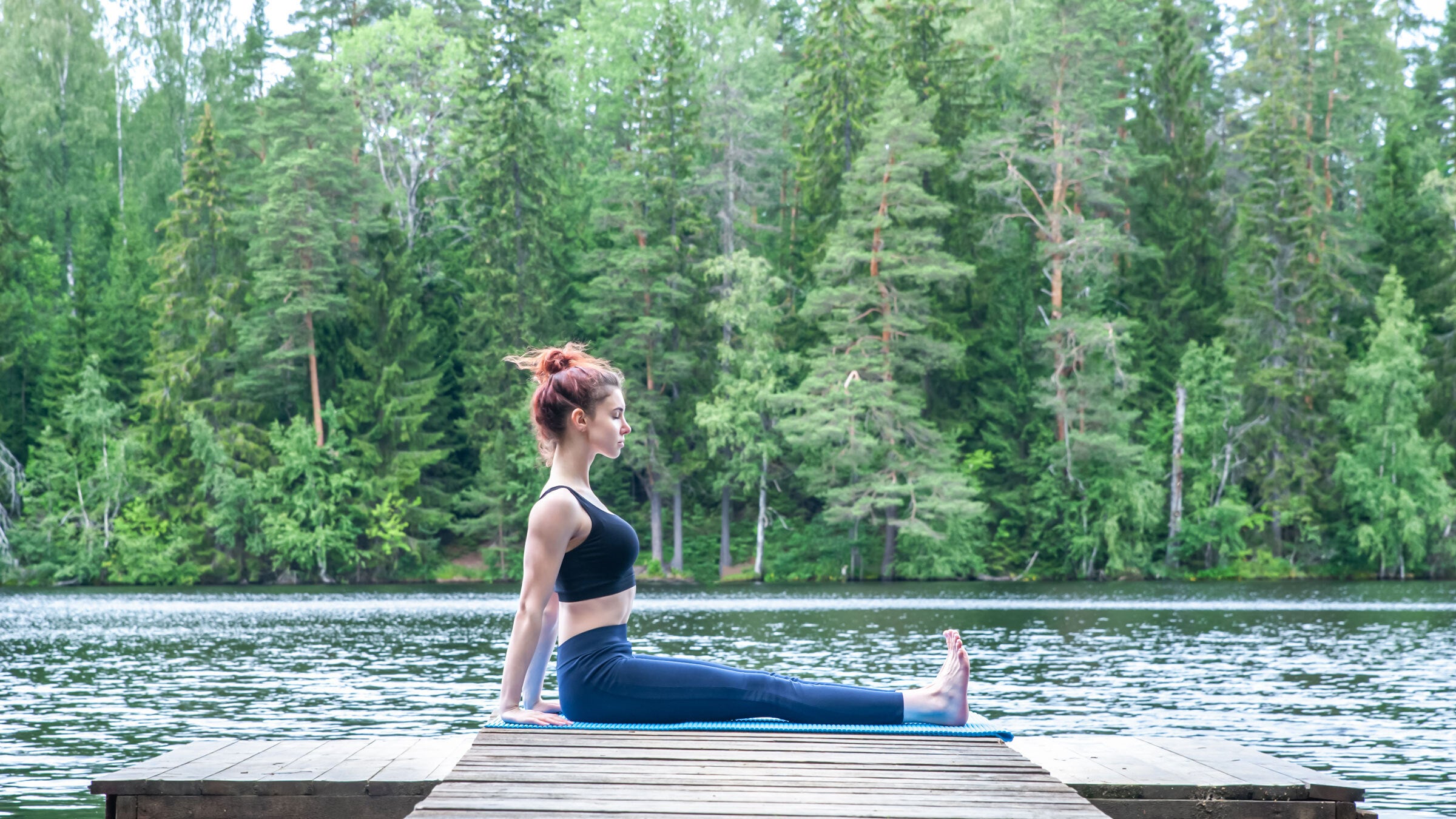 Woman sitting on a yoga mat near a river practicing core strength moves