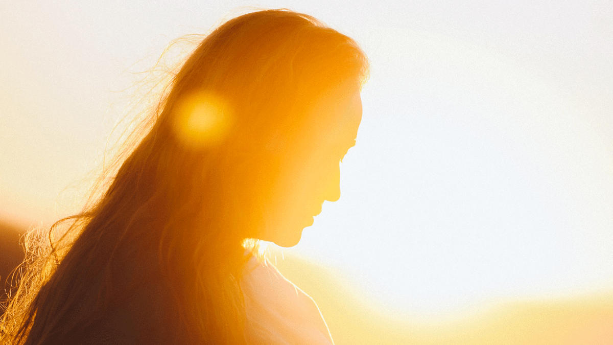 Woman standing outdoors in the Sun looking down and contemplating Venus retrograde