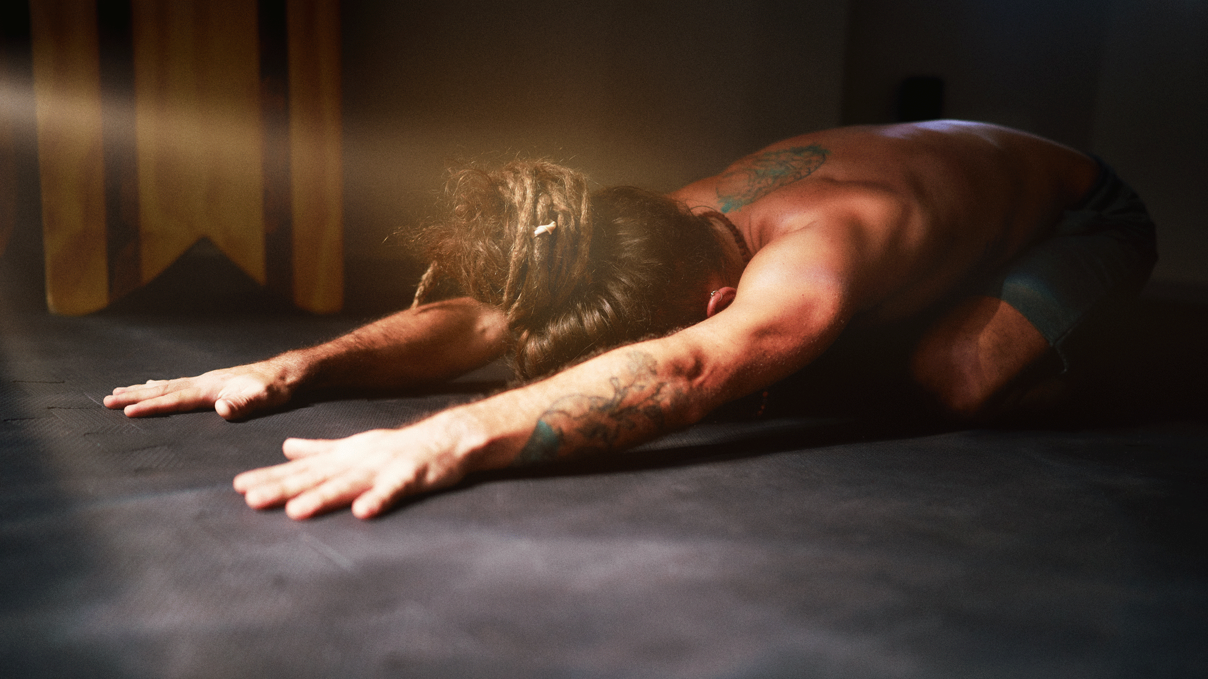 Man with tattoos on his yoga mat practicing Child's Pose