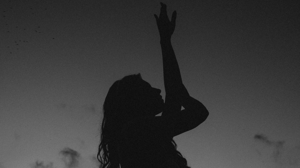 Woman standing outside beneath the new Moon in Leo during August 2023 with her arms lifted toward the heavens