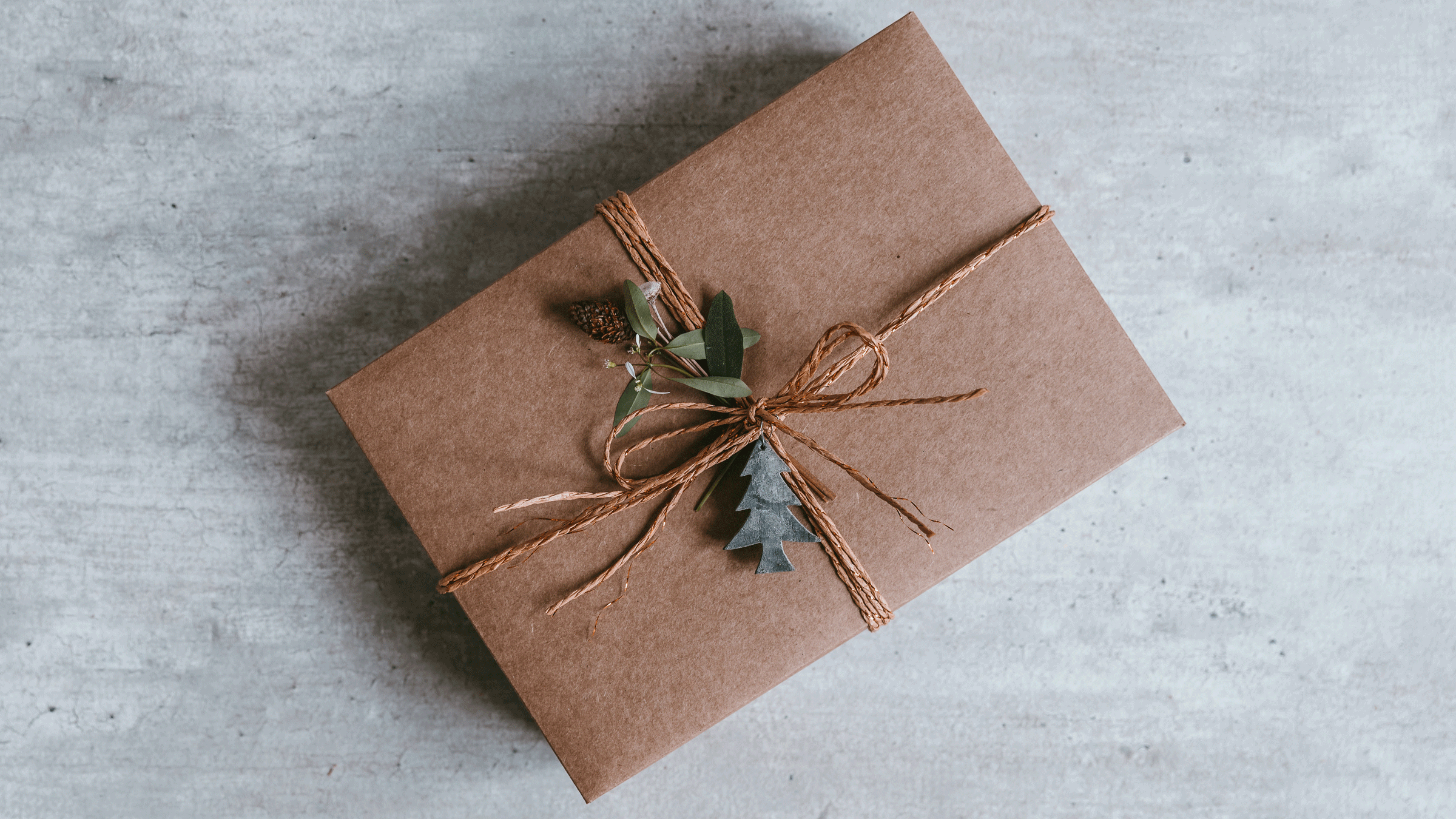 Image of a yoga gift wrapped in brown kraft paper with a delicate twine and leaves of holly