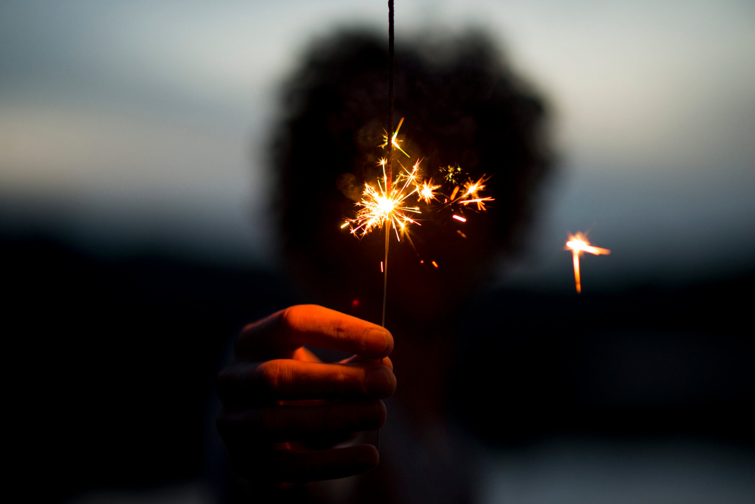 A woman holding a sparkler at dusk contemplating her weekly horoscope