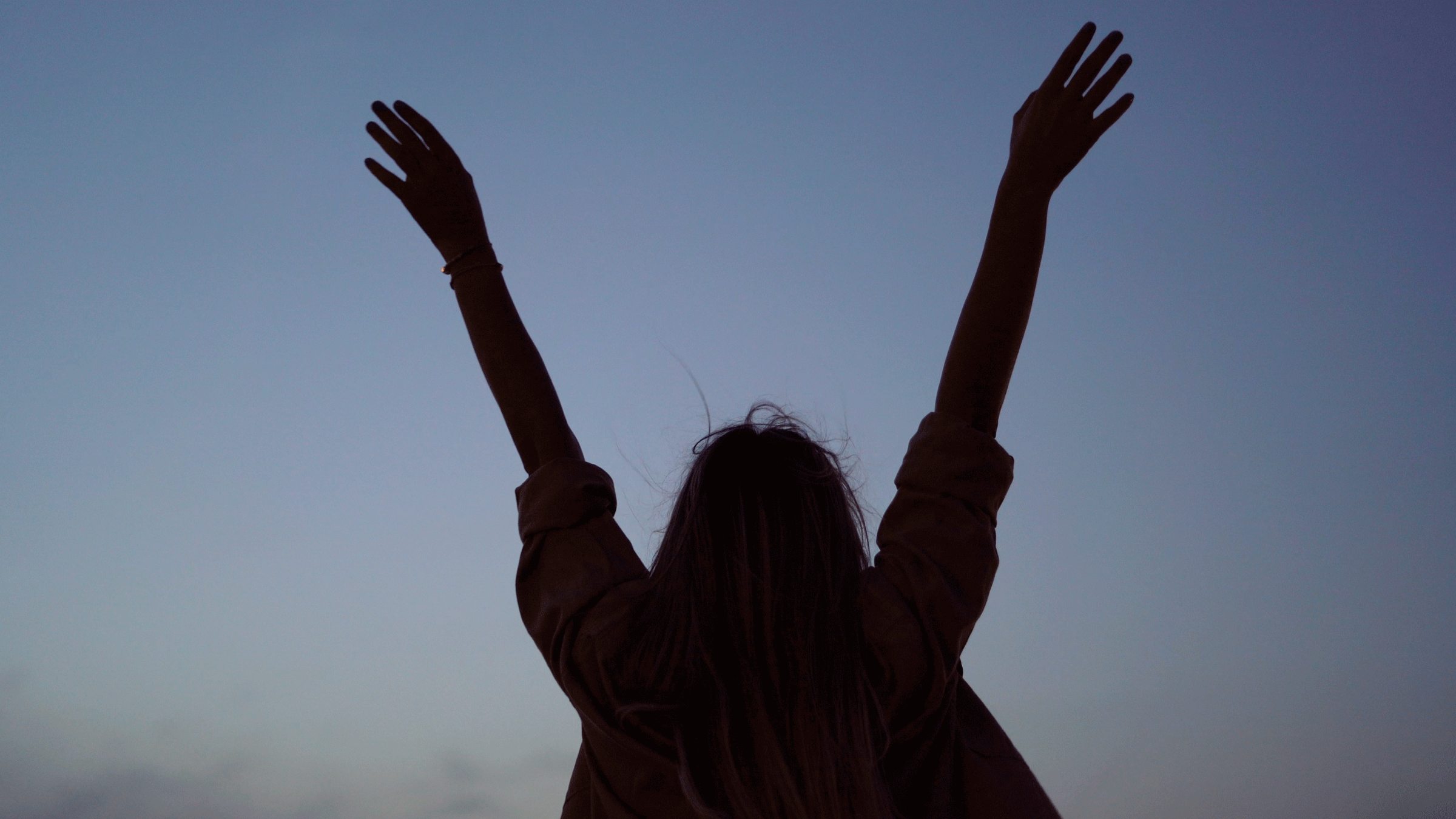 Woman standing outside at night beneath the full Moon in Sagittarius with her arms in the air.