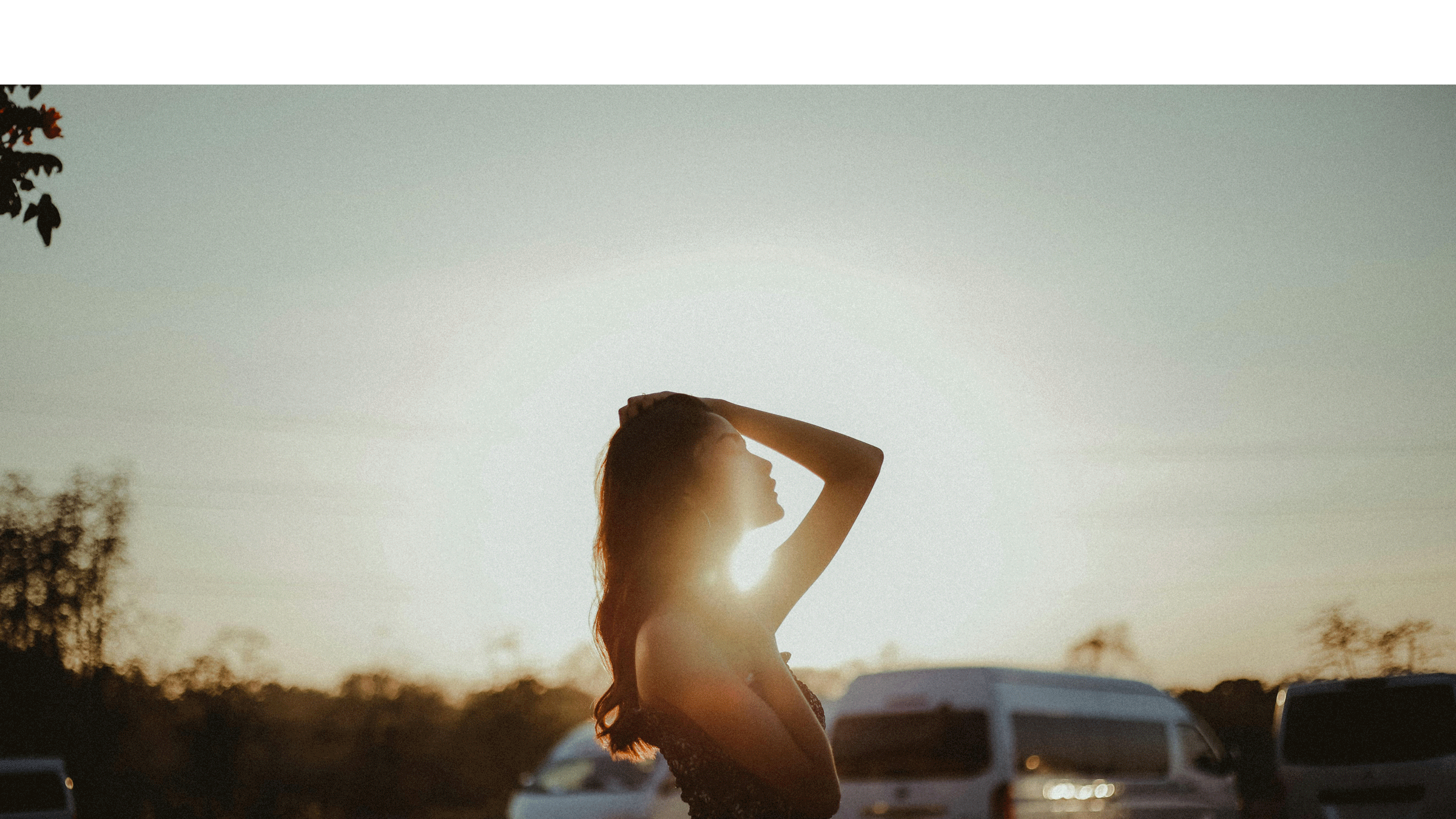 A woman standing outside before dusk by an old pickup with the sun behind her as she contemplates her weekly astrology forecast.