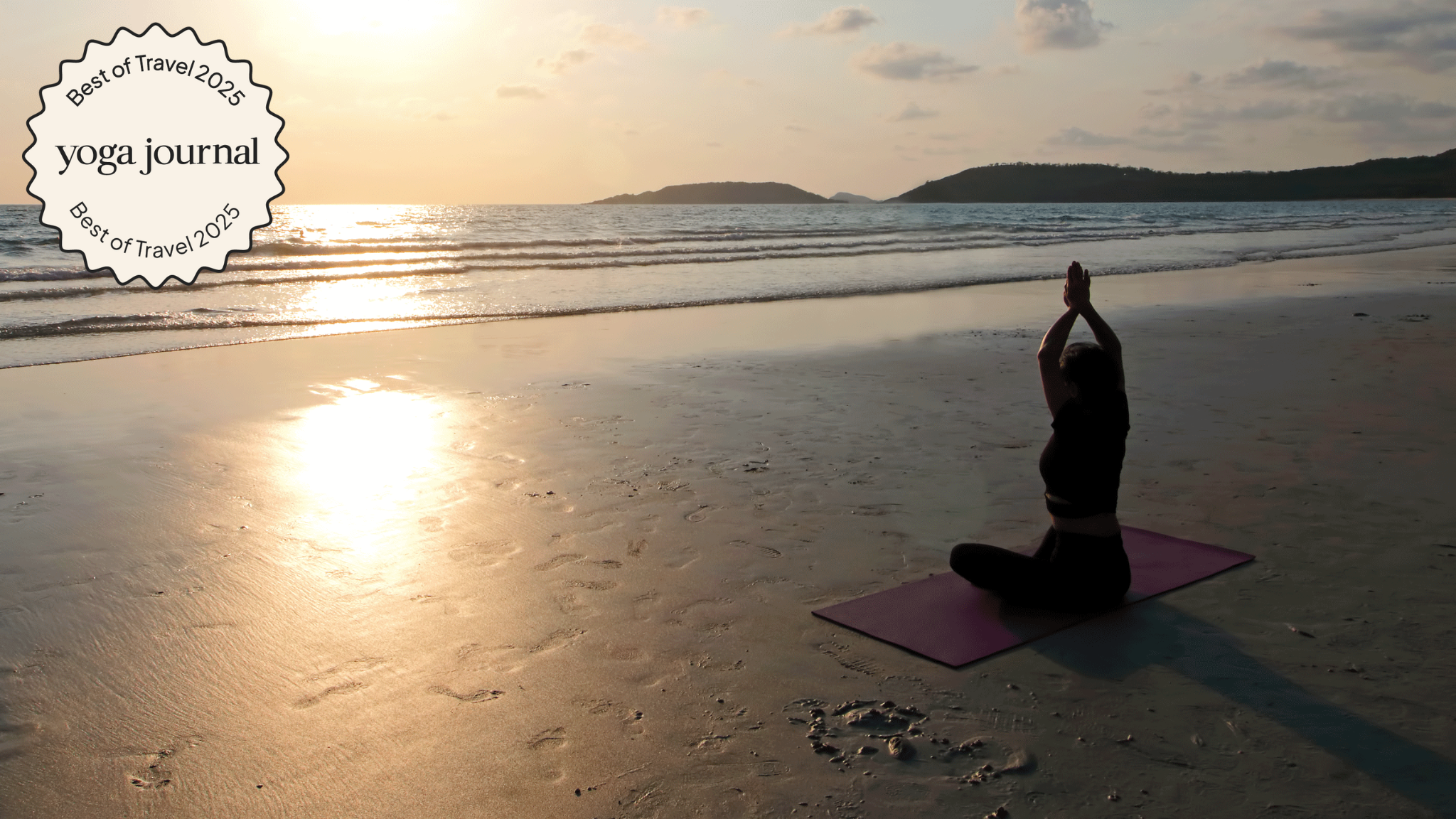 Person practicing yoga outdoors on the beach as the sun sets over the ocean.