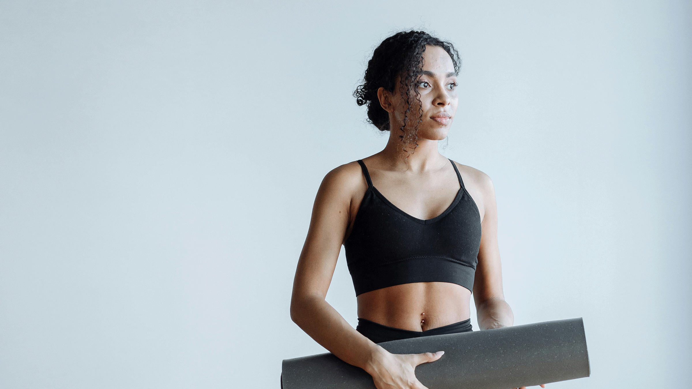 Woman standing in a yoga studio holding her rolled up mat