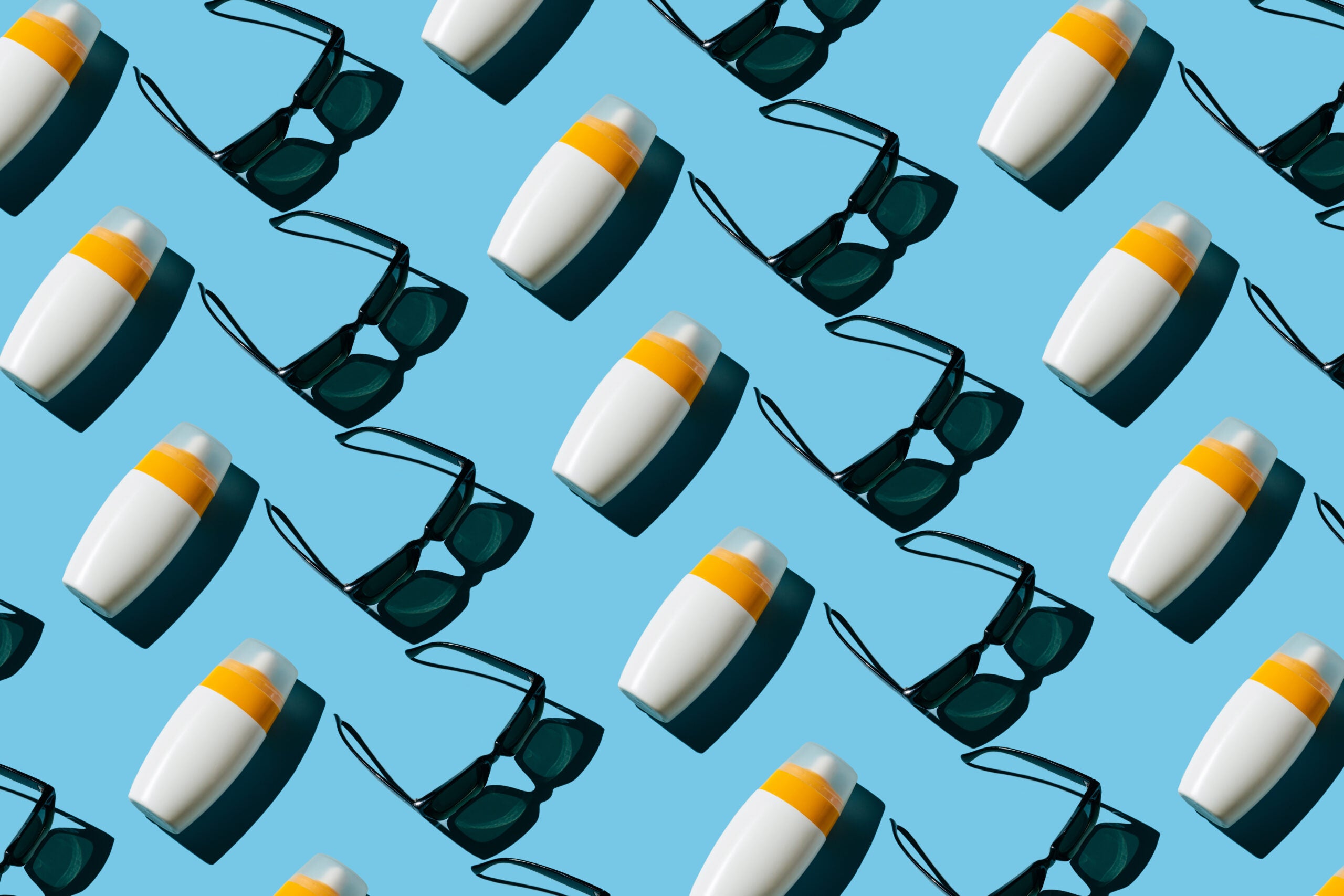 Pattern of black sunglasses and white bottles of sunscreens against a sky blue background.