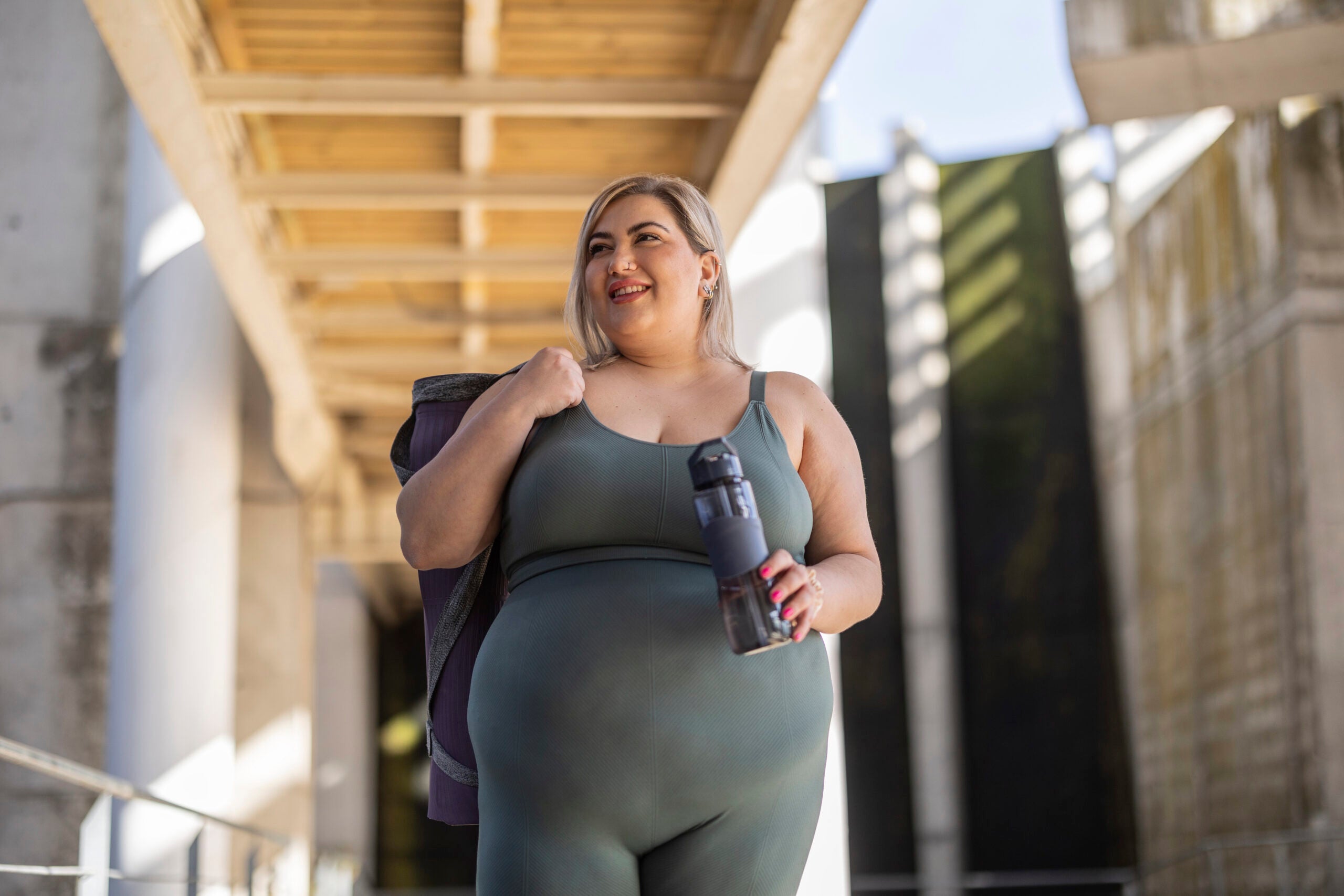 Woman standing with exercise mat and water bottle.