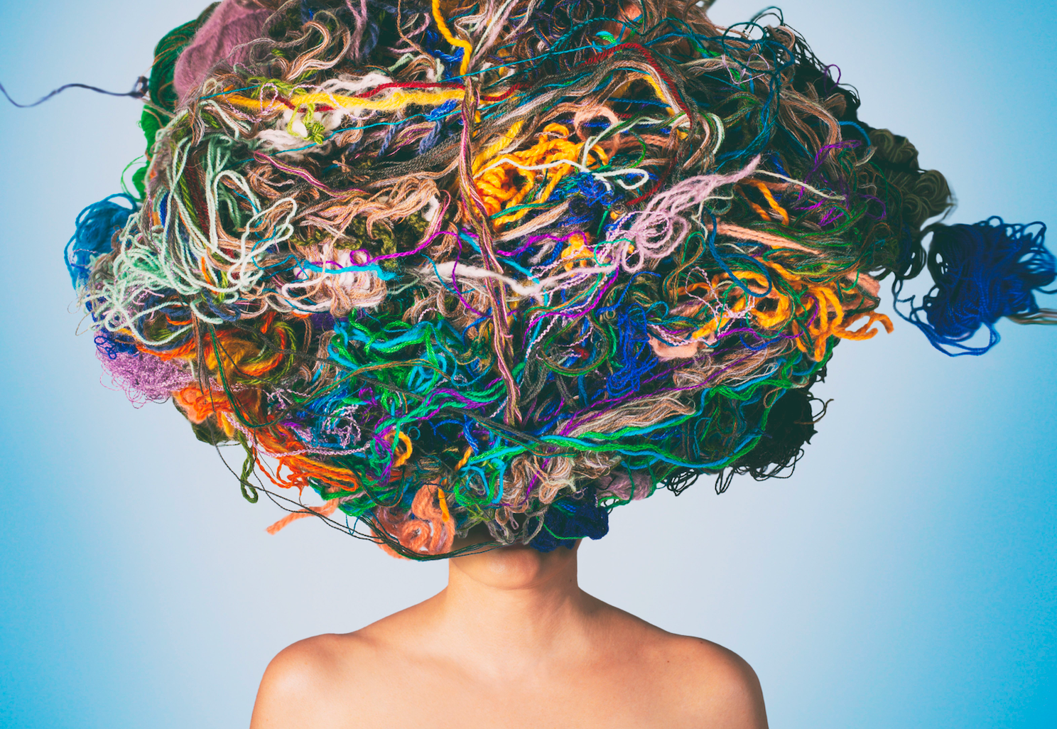 Conceptual image of a person's shoulders and head covered by a mangled clump of multi-colored yarn.