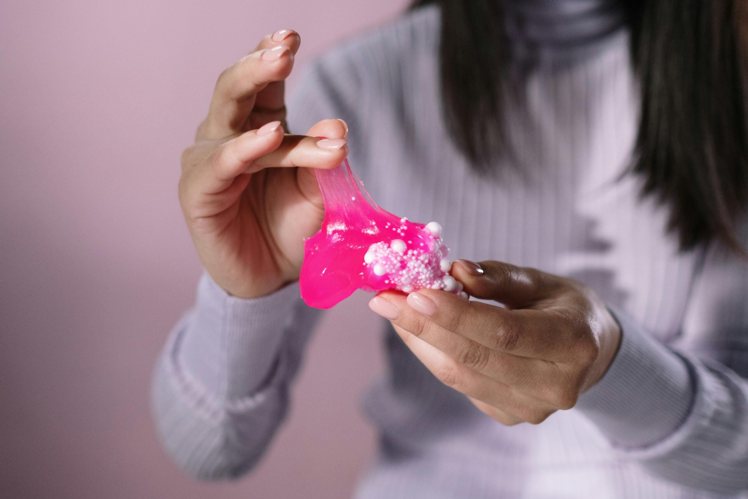 What kind of slime is best for stress relief? Close-up of woman's hands playing with glop of pink slime.