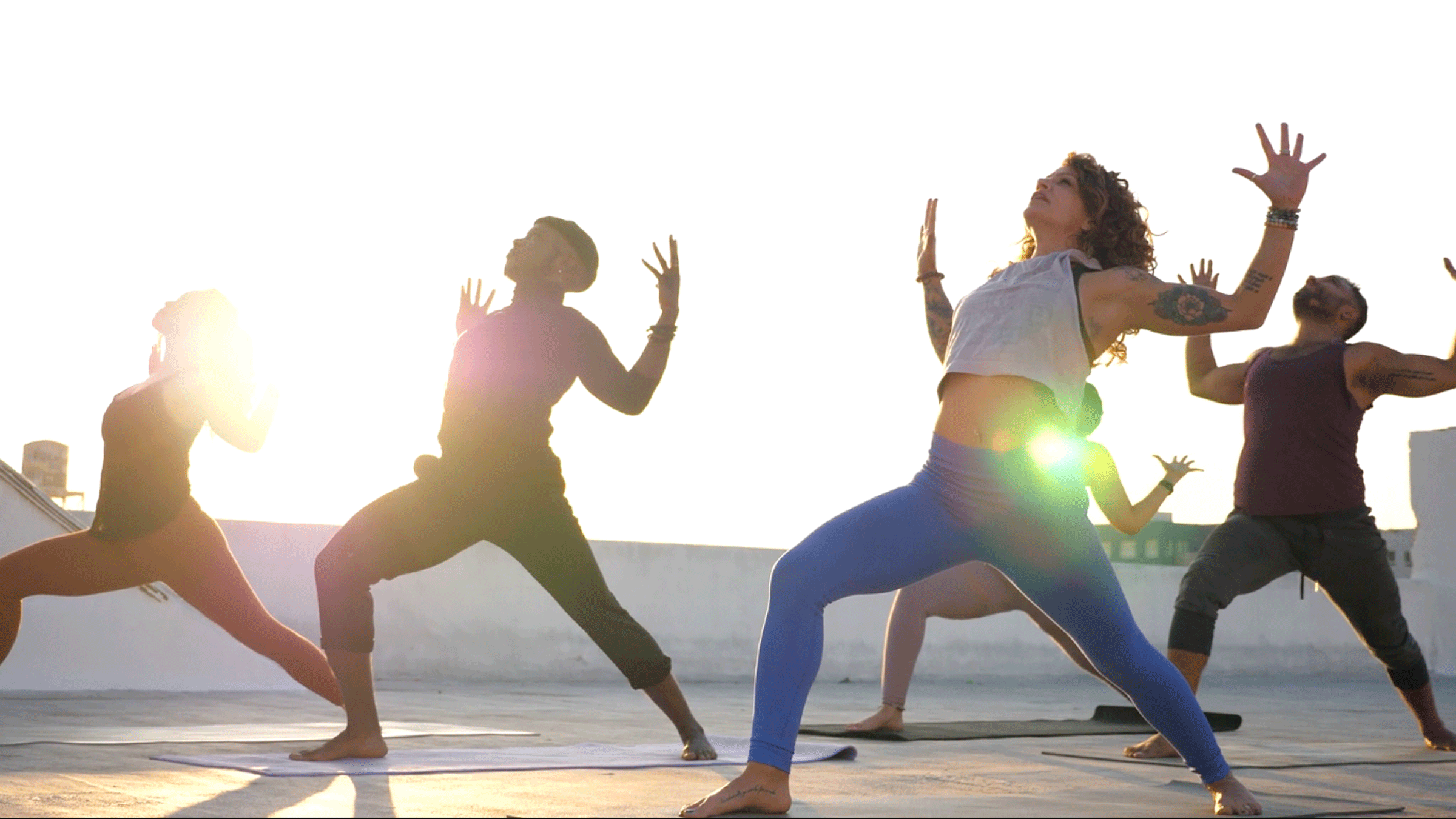 Yoga class on an outdoor rooftop with students in Warrior 1 while the teacher shares yoga cues