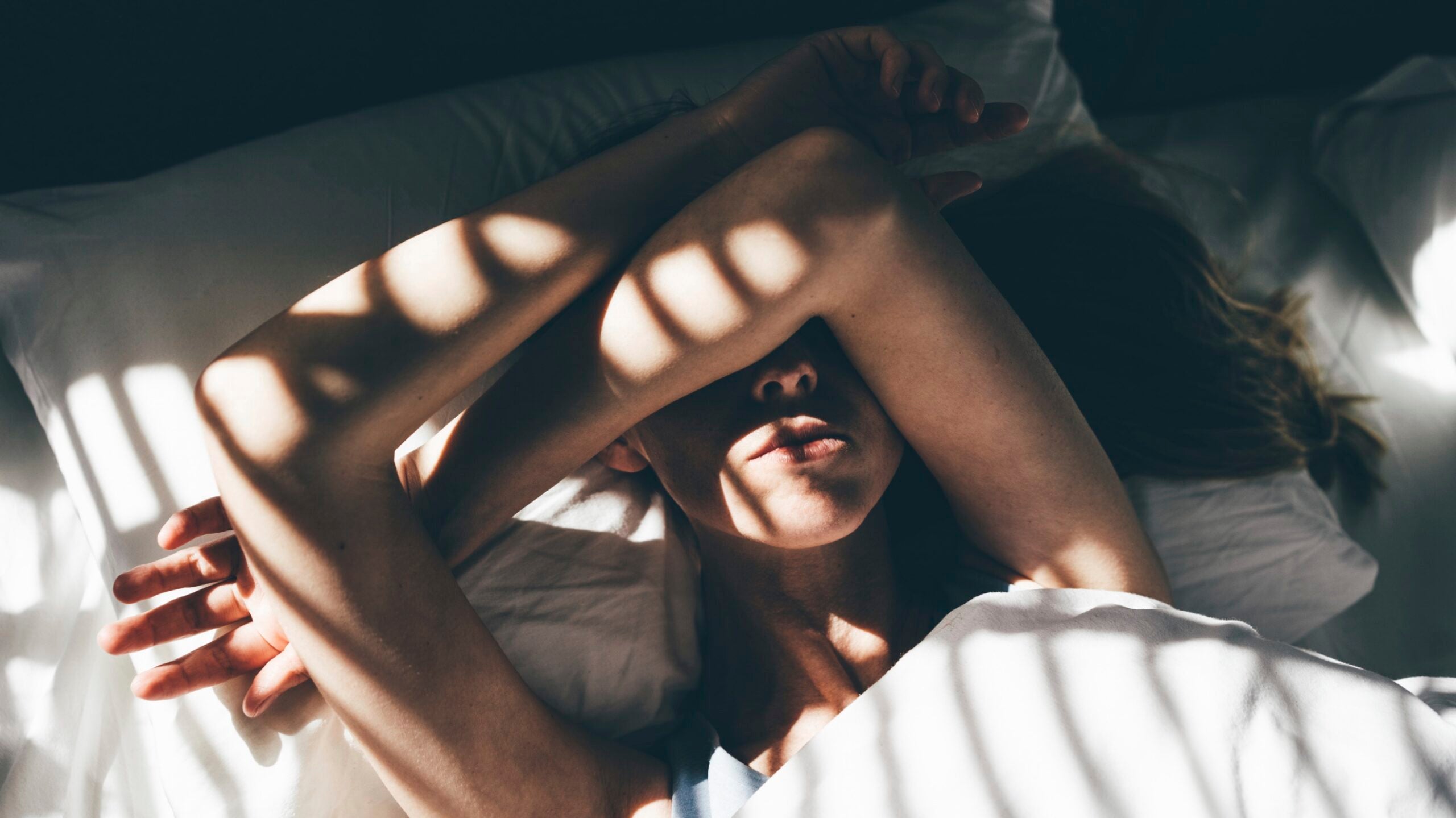 Yoga teacher in bed not wanting to teach class with her arm over her eyes