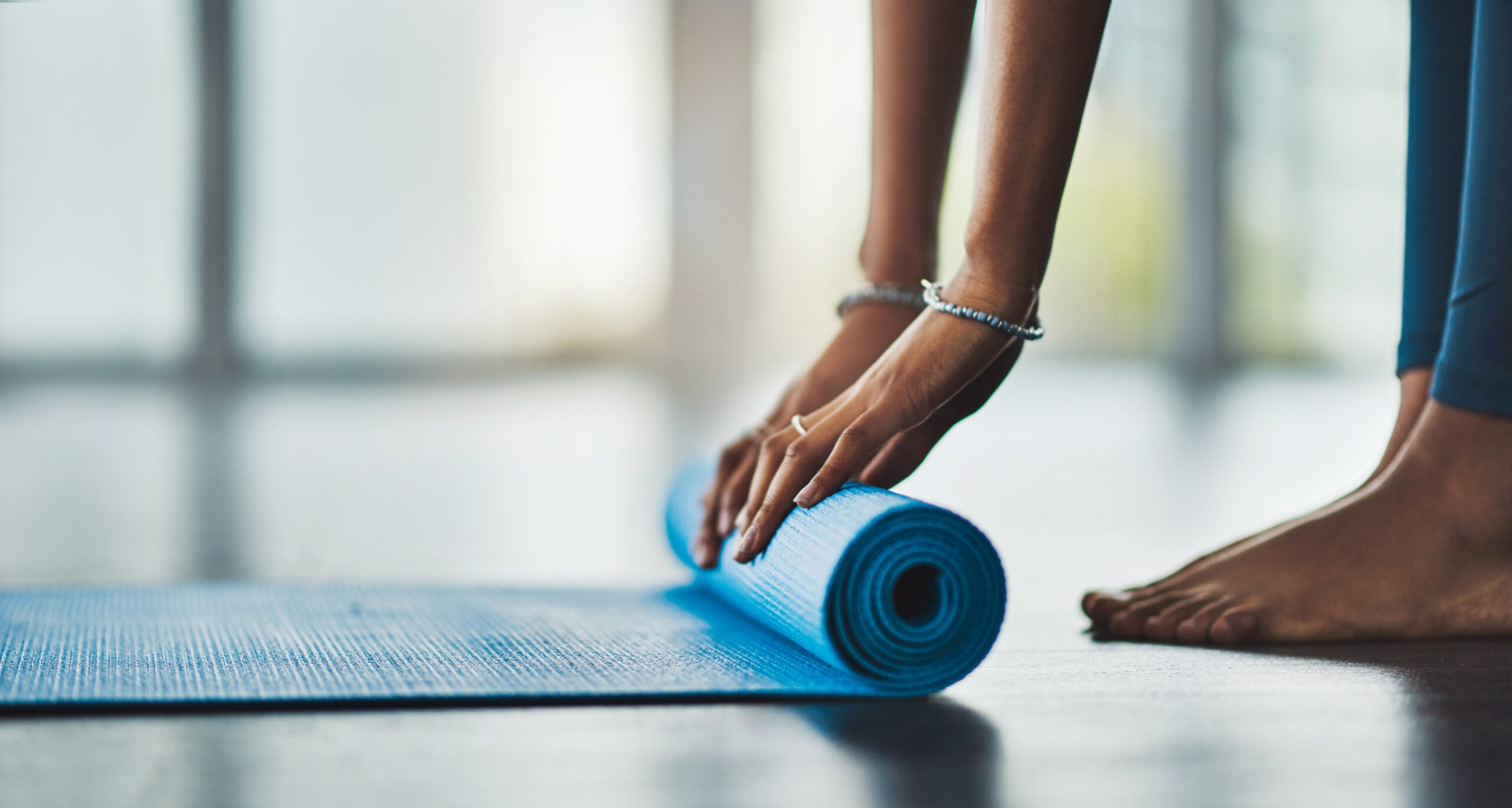Woman rolling up blue yoga mat.