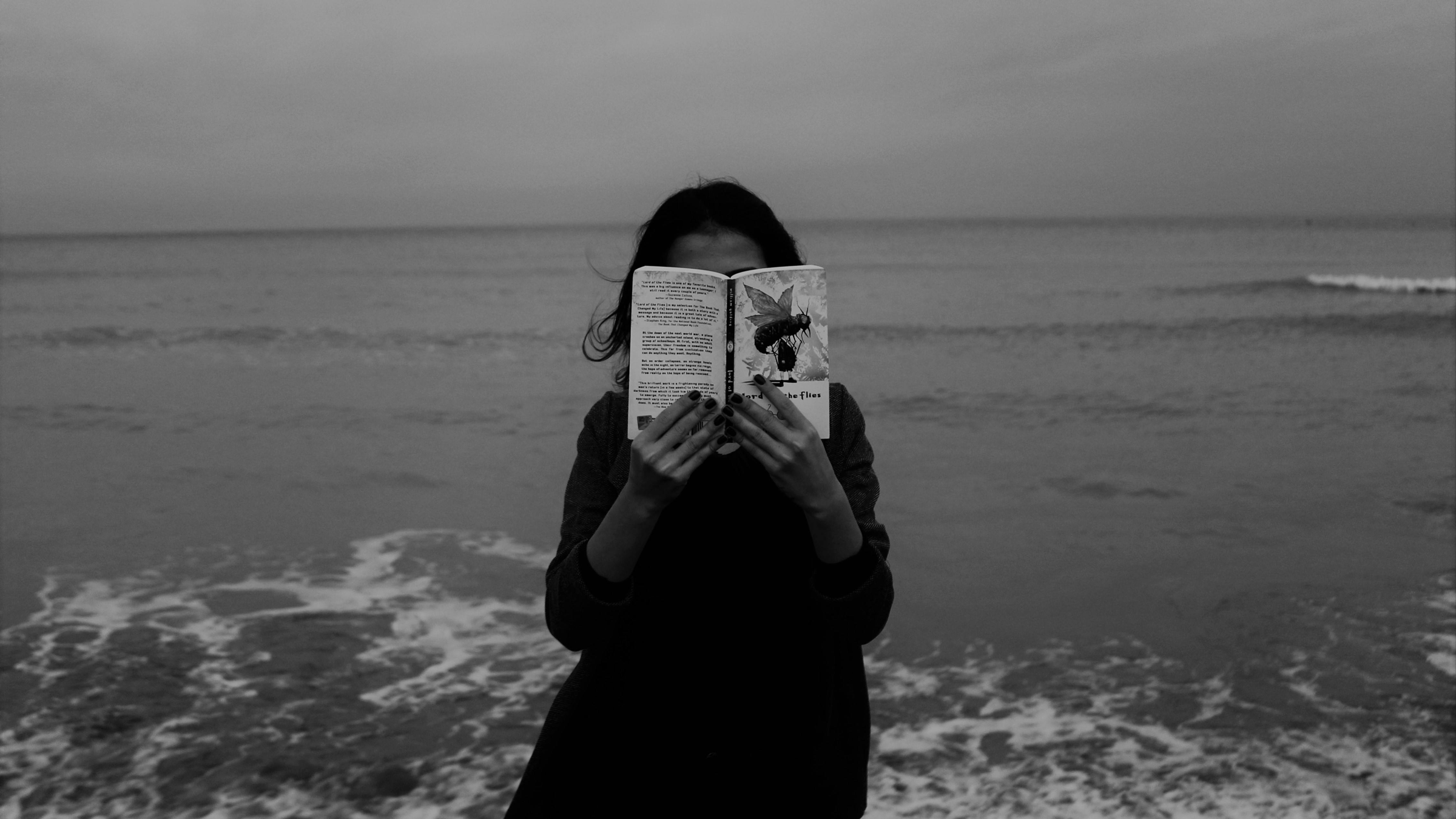 Woman sitting and reading by the ocean while thinking about her weekly horoscope for January 5-11, 2025