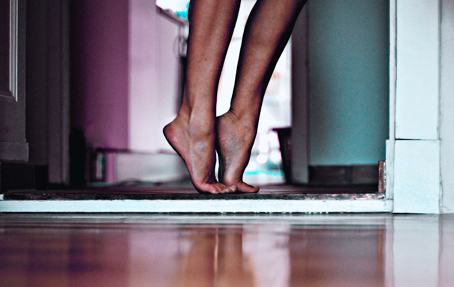 Barefoot woman standing in a doorway on a hardwood floor practicing ankle-strengthening exercises Miss K.B. Photography