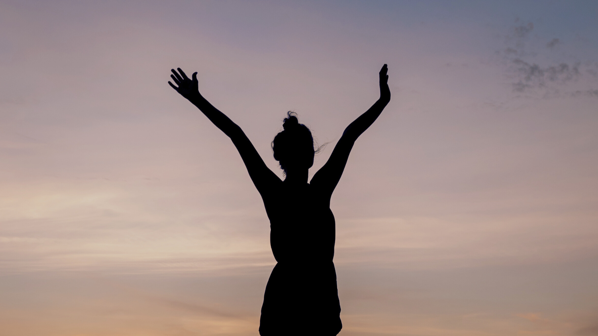 Woman standing outside with her arms outstretched at dusk