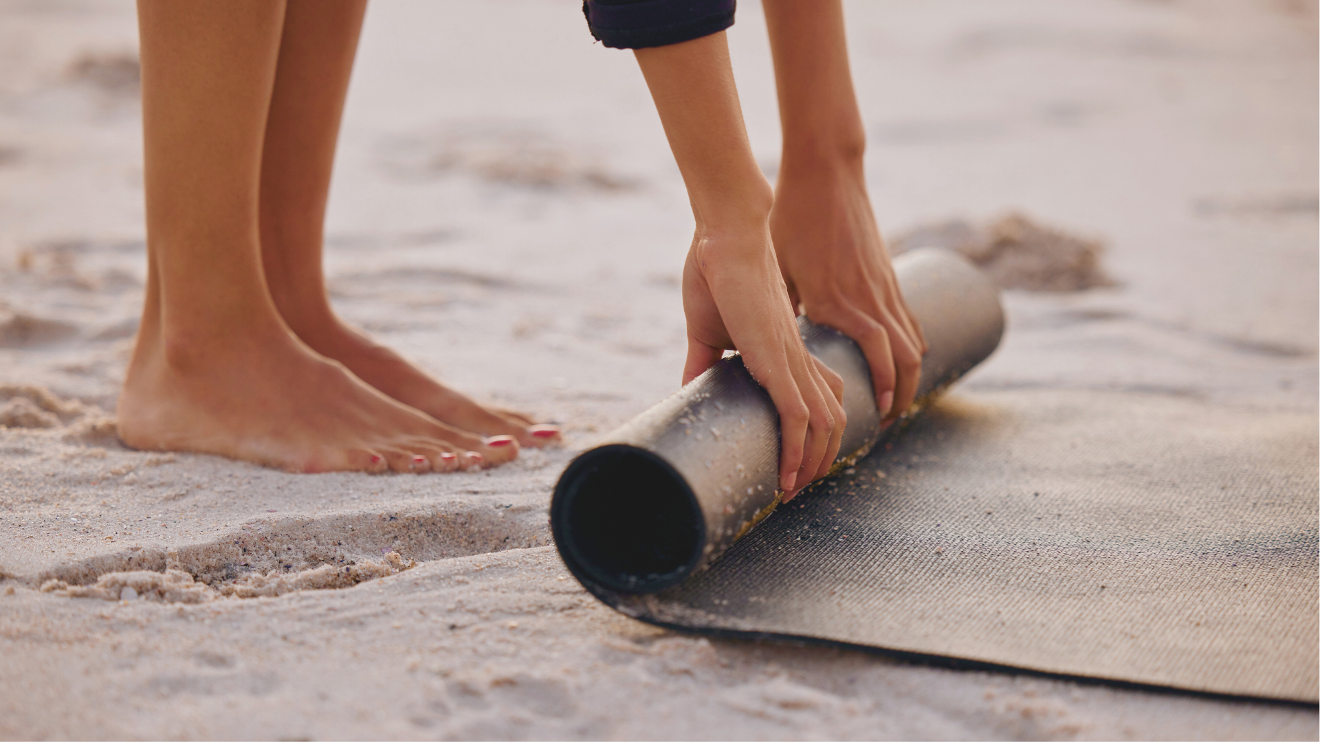 Woman standing on a beach rolling up an eco-friendly yoga mats on the sand