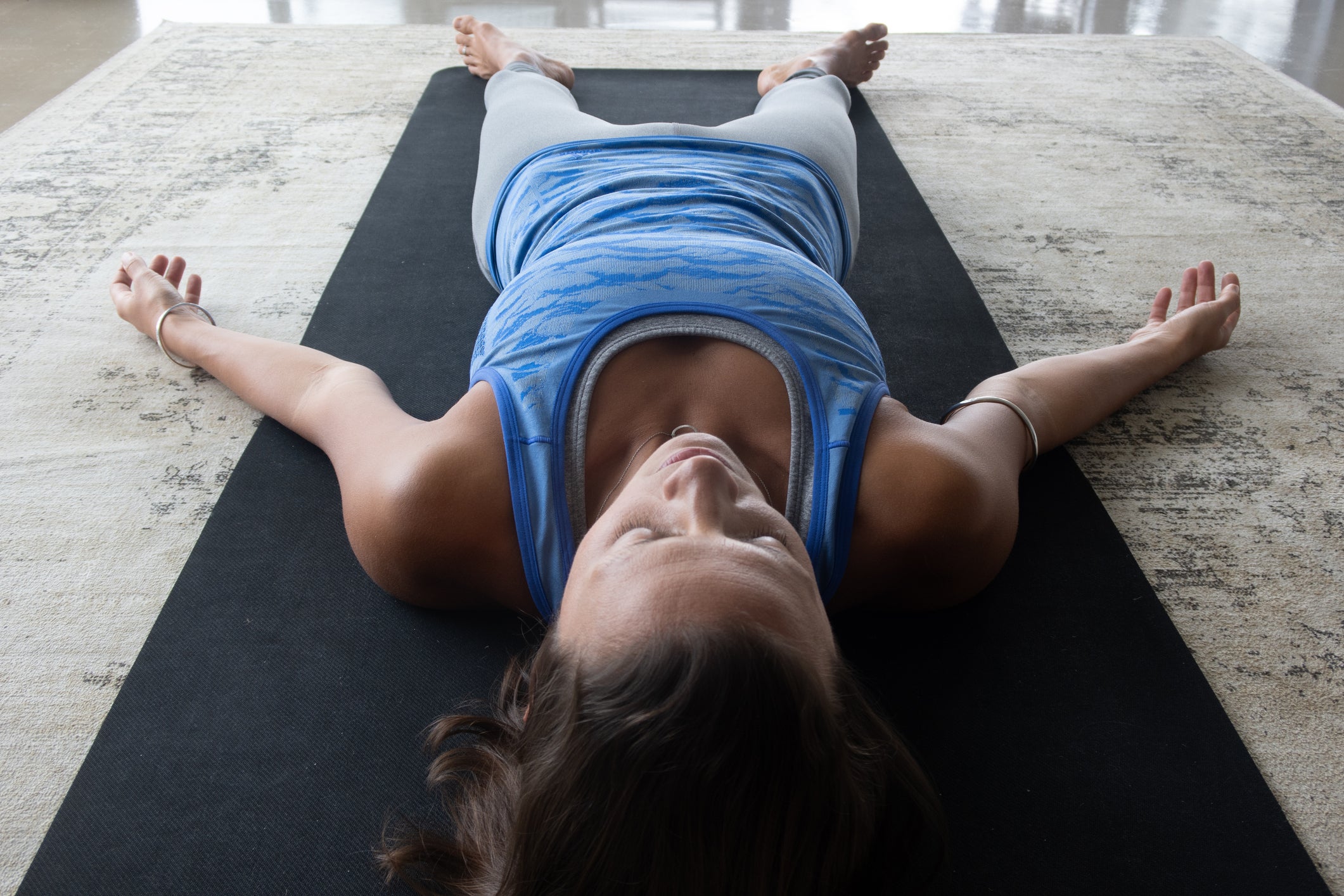 Yoga student or teacher laying down in resting position on her mat dressed in blue yoga leotard or exercise clothing in a clean environment in studio or at home.