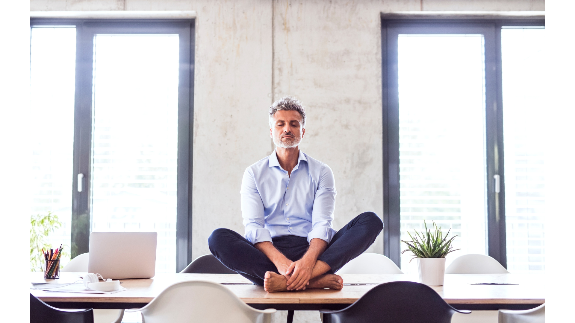 Man sitting cross-legged on a desk in an office practicing desk yoga