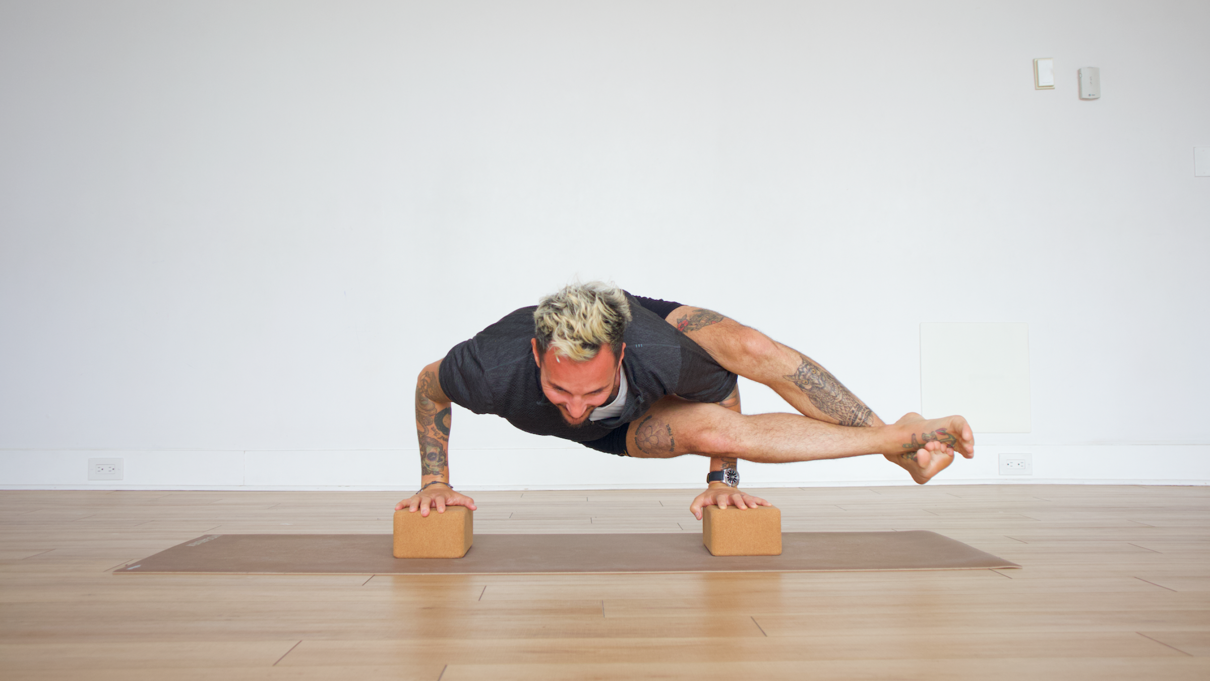 man in eight angle pose on blocks on yoga mat