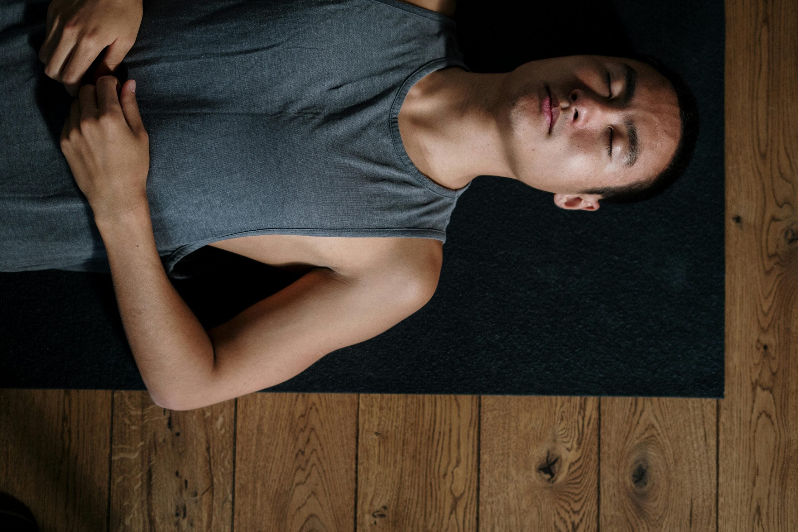 Man lying down on black yoga mat with eyes closed.