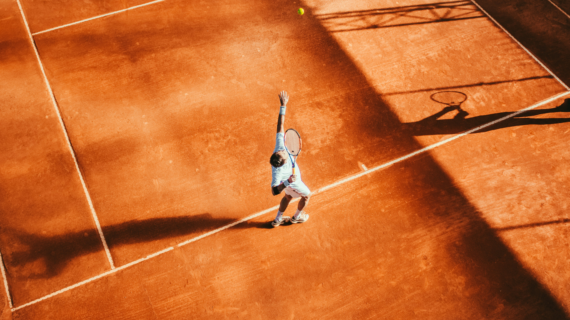 Tennis player on a clay court about to serve after practicing strength training exercises for tennis