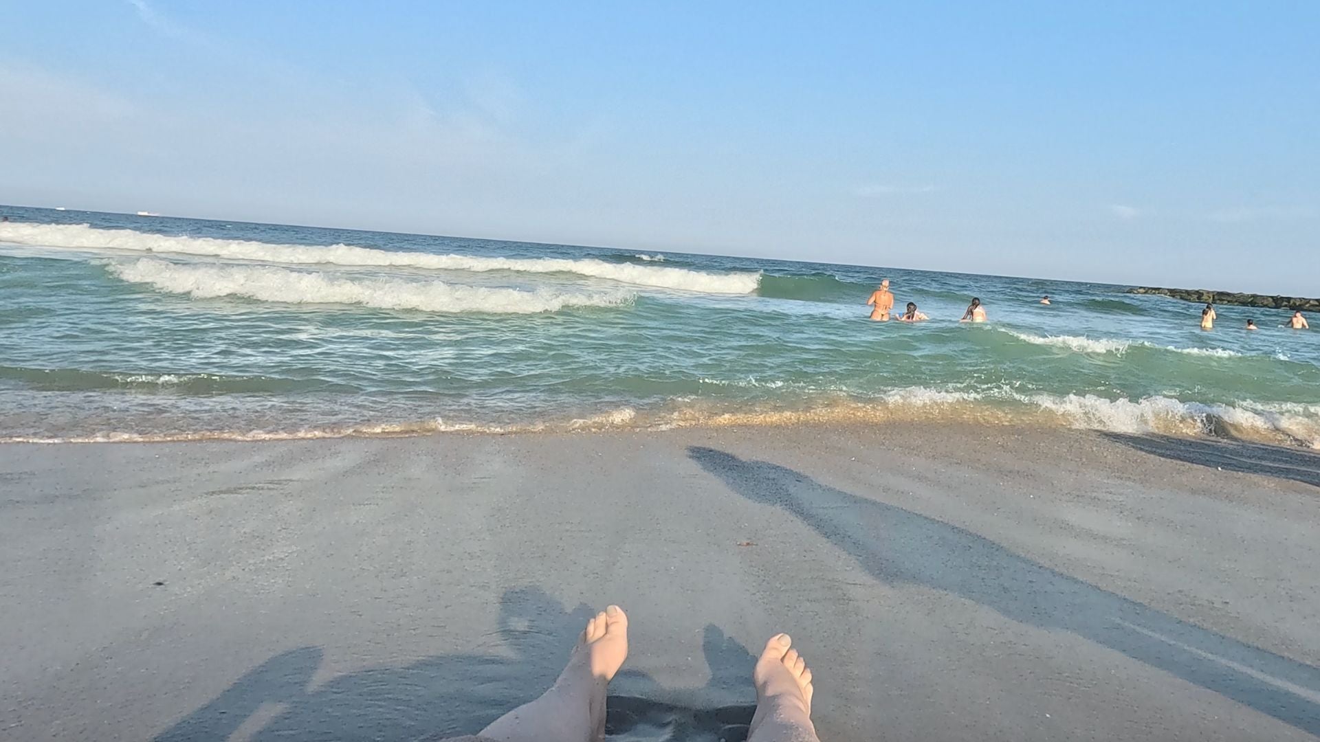 Image of person's feet on the beach with blue waves and sky in the background.