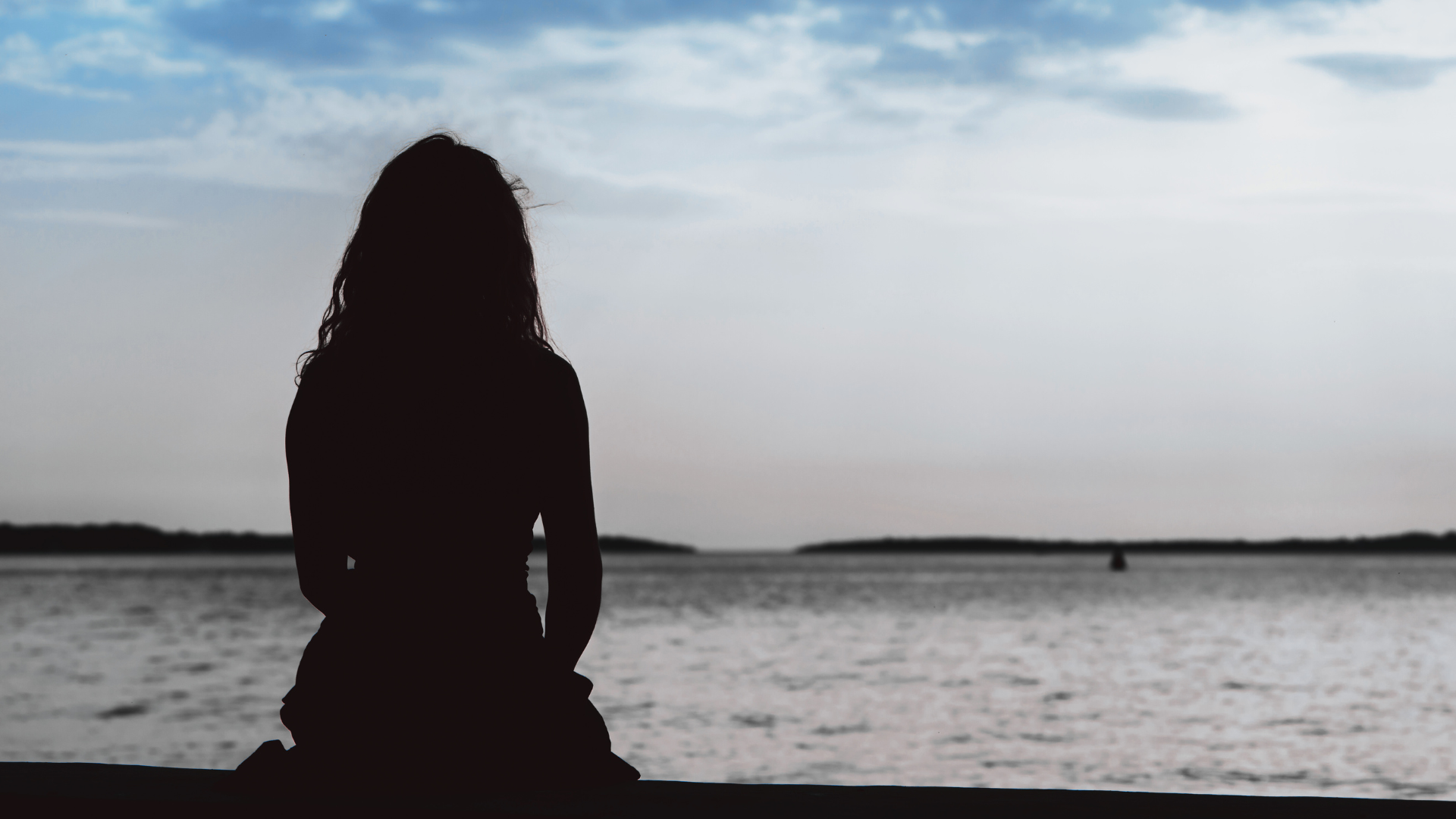 Woman silhouette sitting on the beach by the sea contemplating her weekly horoscope for July 27-August 2, 2025