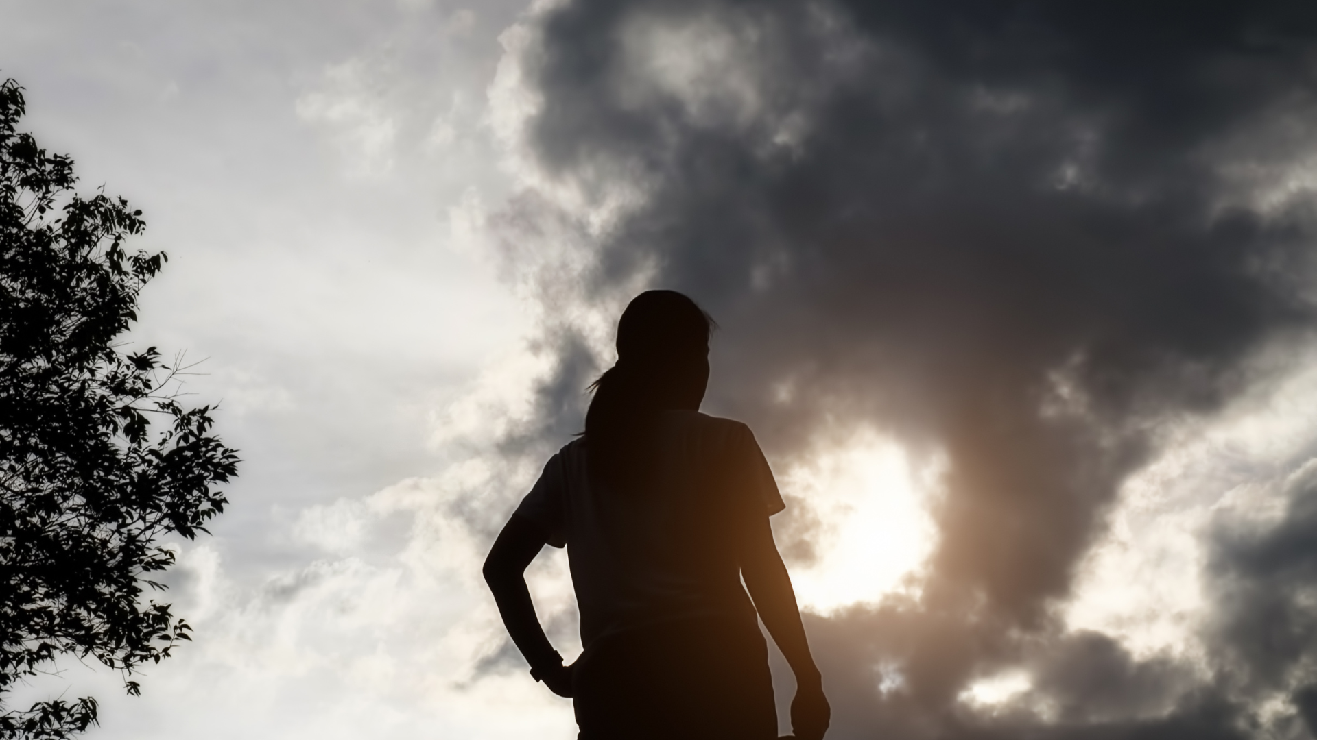 Woman standing outside under a tree in summer watching the sunset and contemplating the weekly horoscope for early July 2025