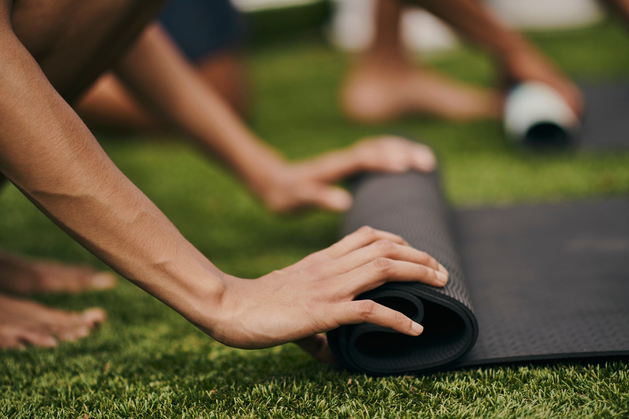 An unrecognized couple in their garden at home is busy rolling up their yoga mat as they finish up their morning exercise routine. Stock photo