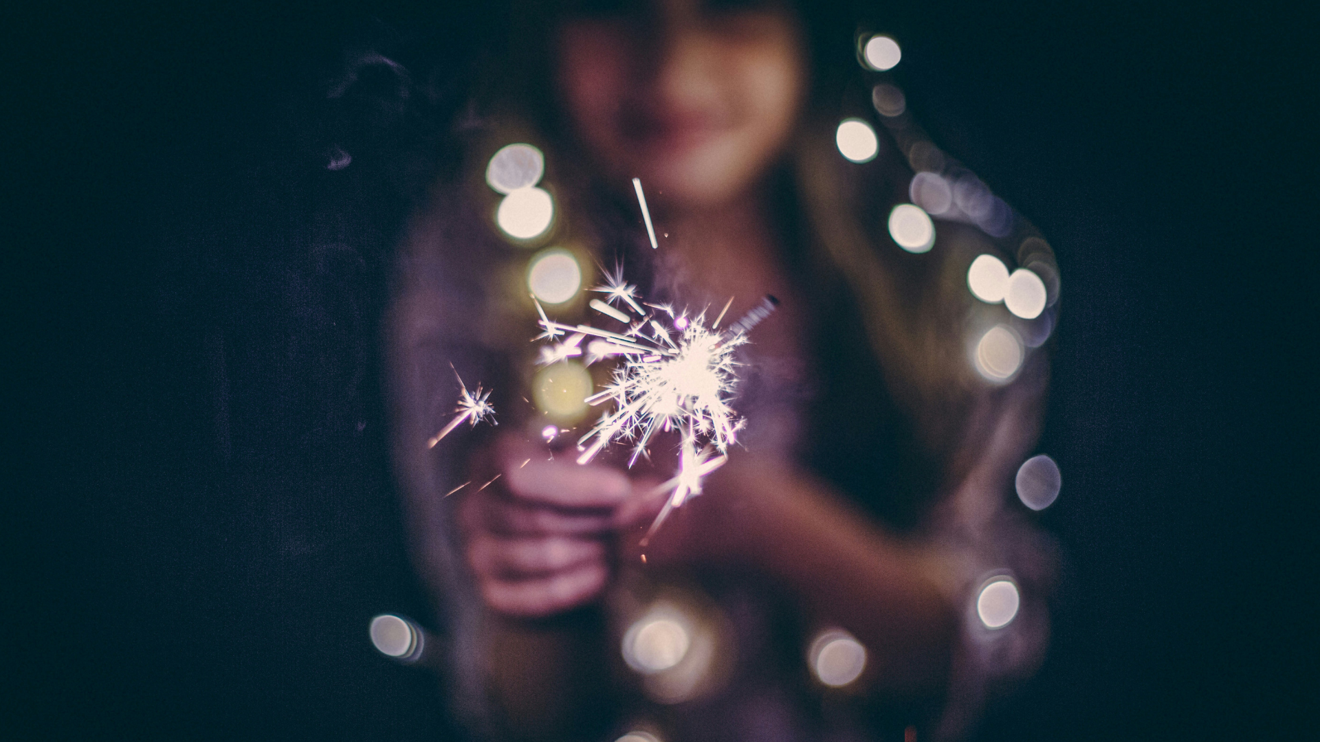 Girl holding sparkers and twinkle lights at night