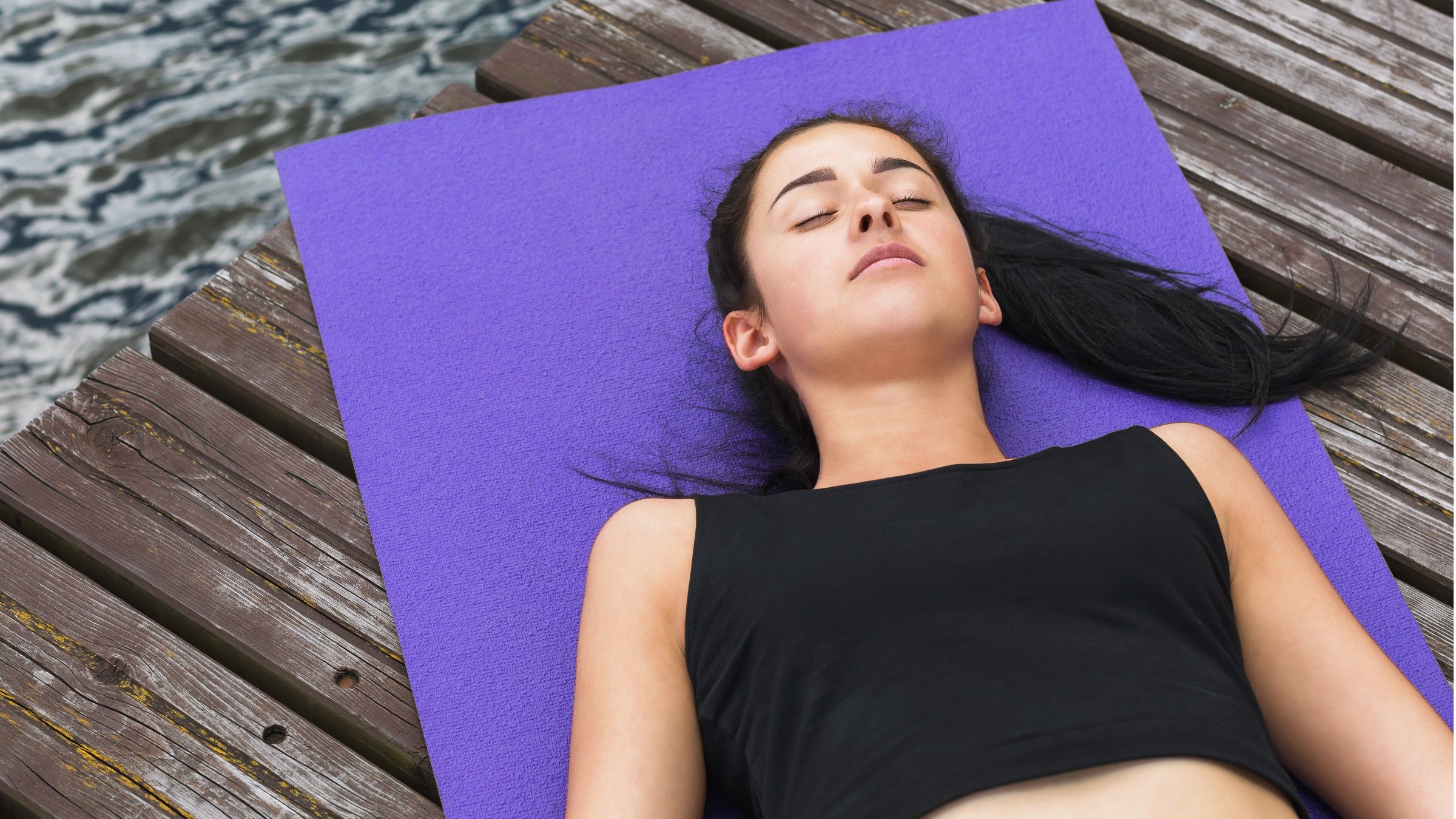Woman lying in corpse pose on mat near river