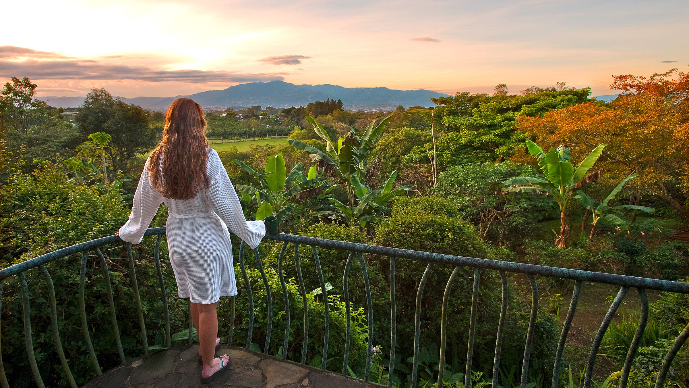 Woman stands on balcony overlooking Costa Rica at sunset