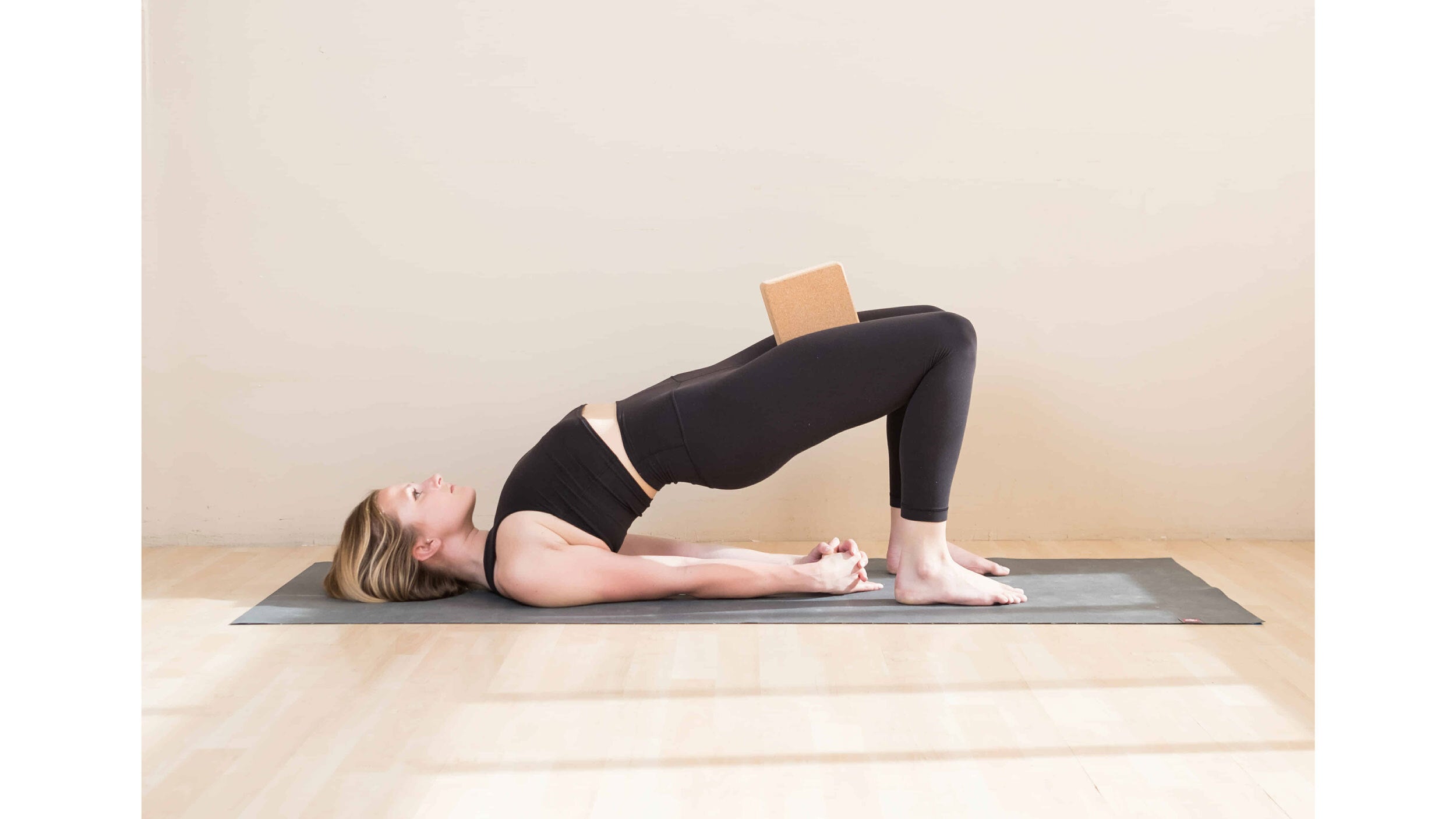 A woman performs a variation of Setu Bandha Sarvangasana (Bridge Pose) with a block